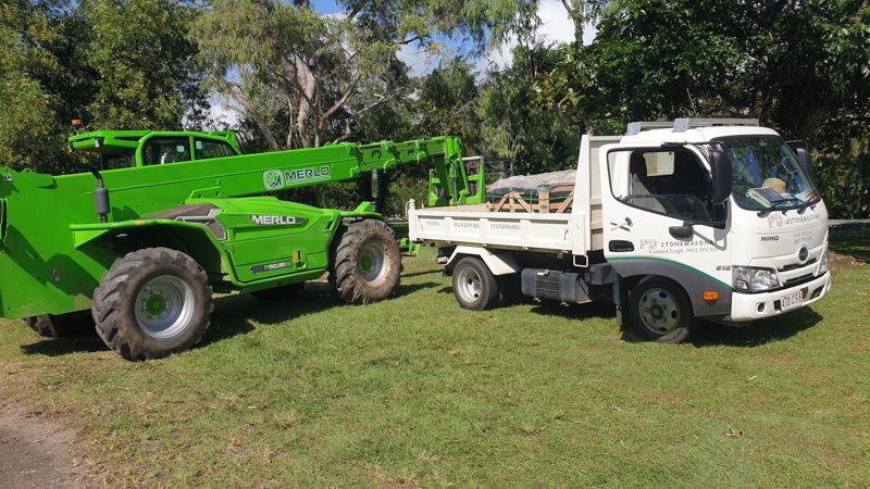 A green crane is towing a white truck in a grassy field.