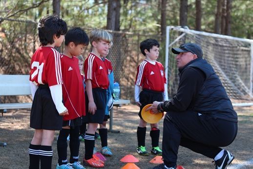 A group of Alpharetta Ambush Soccer Club's young boys are standing next to each other on a soccer field.