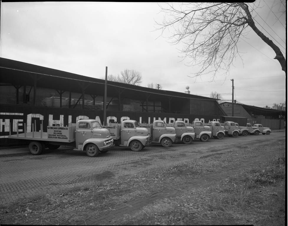 Line of vintage trucks parked beside a long warehouse in black and white
