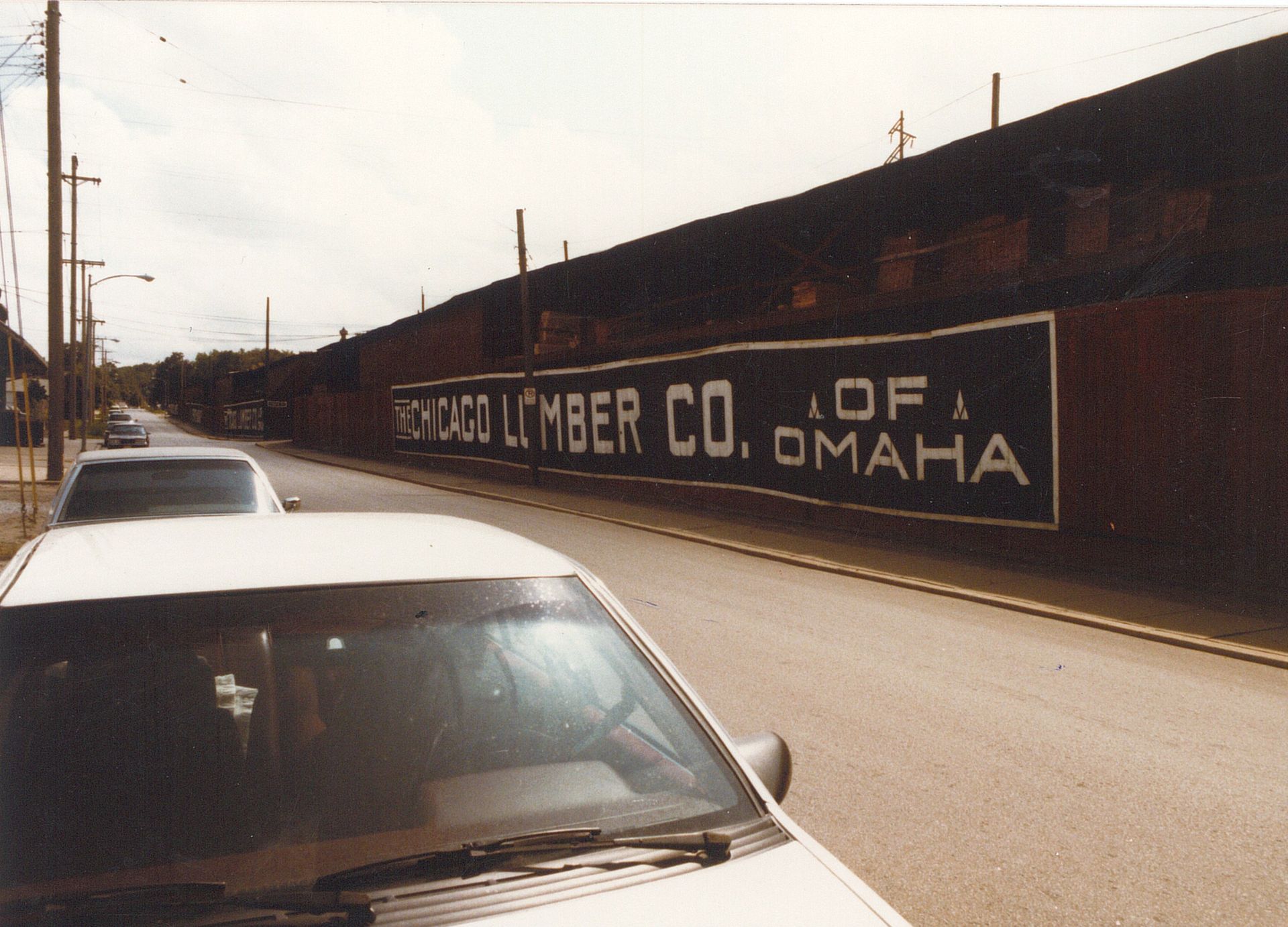 Street view of parked cars beside a long brick wall painted “Hercules Lumber Co. of Omaha”