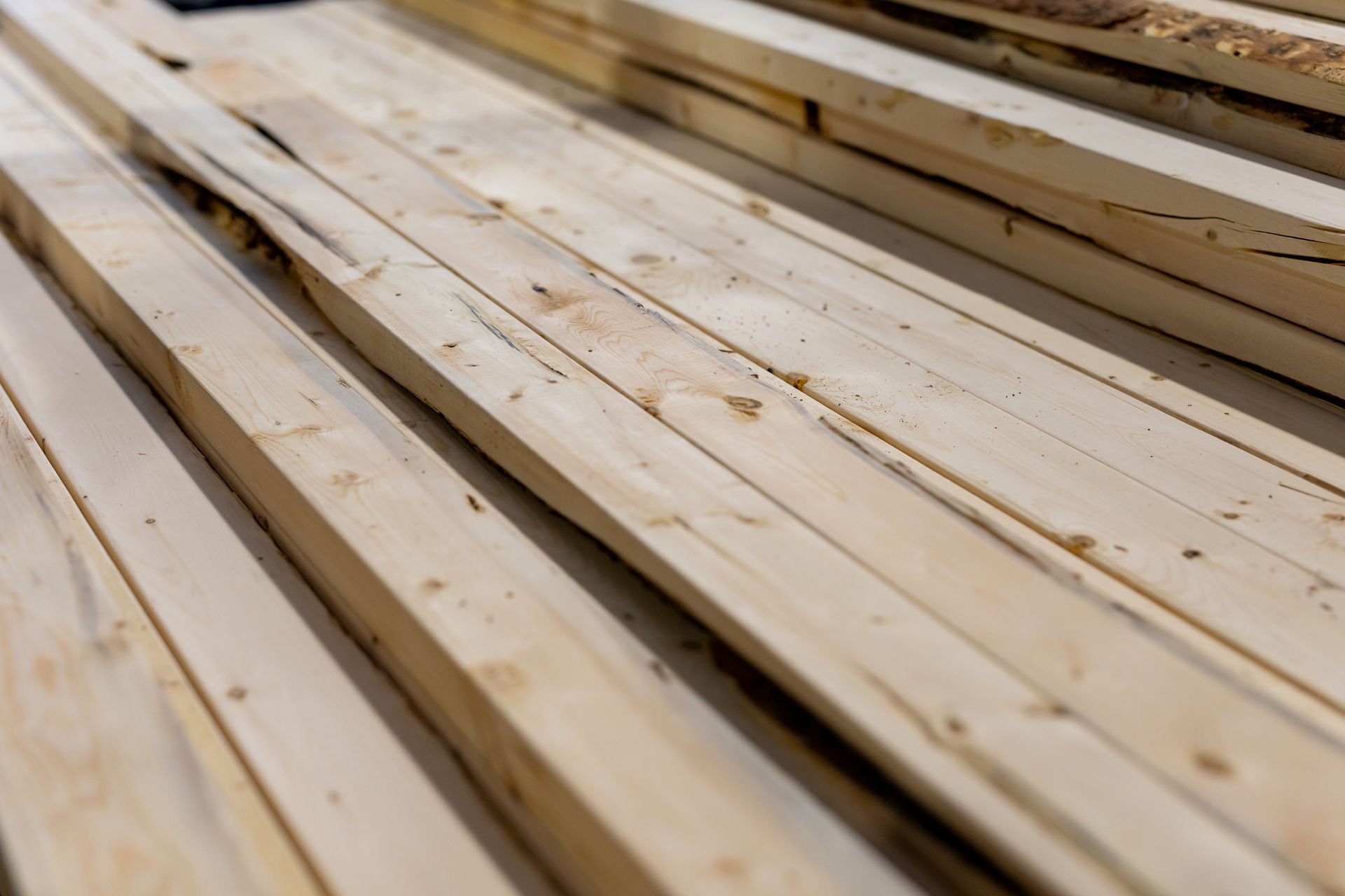 Stacked pale wooden planks with visible knots and grain, viewed at an angle.