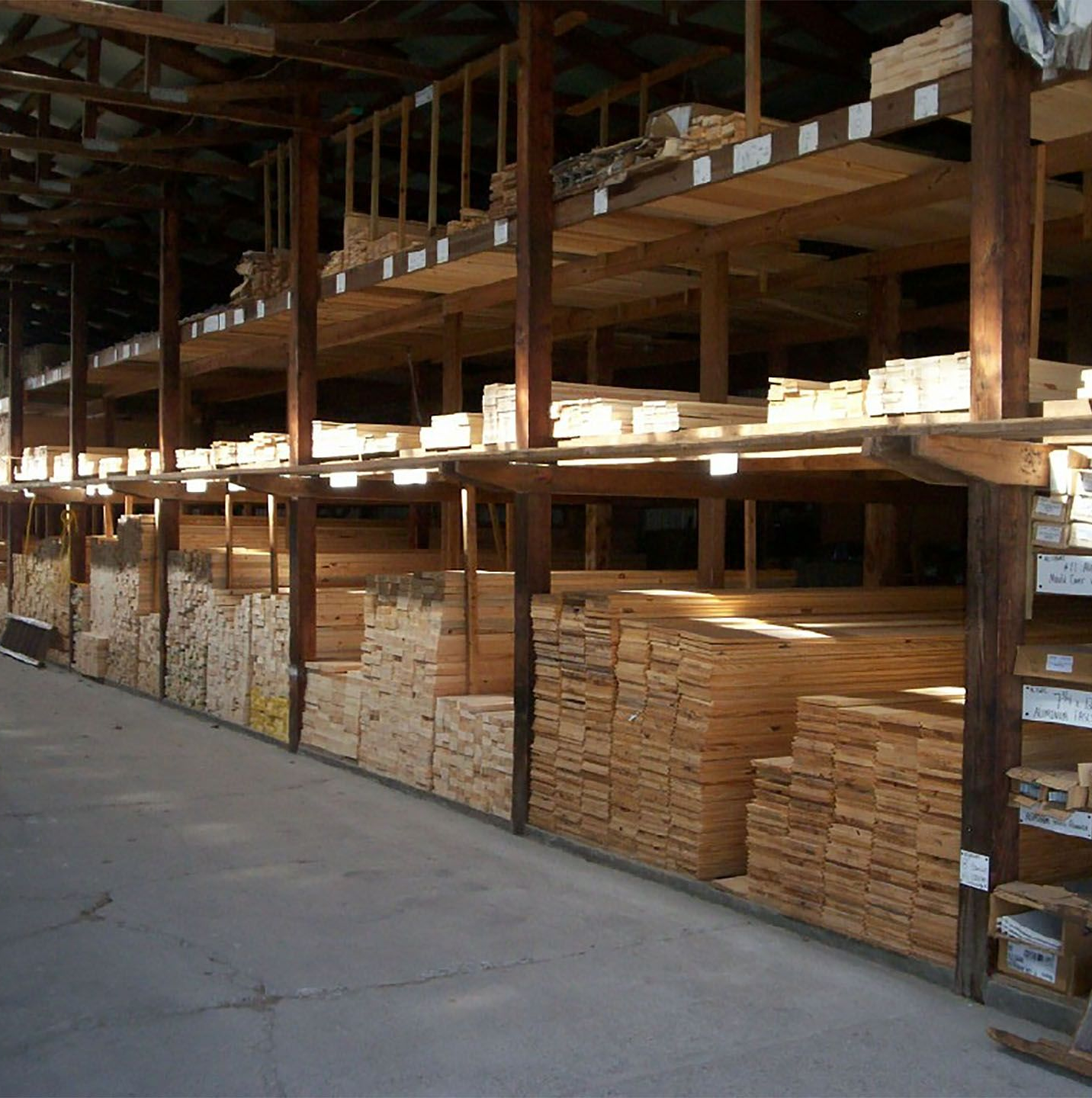 Wood storage warehouse with stacked lumber on multi-tier shelves along a concrete aisle