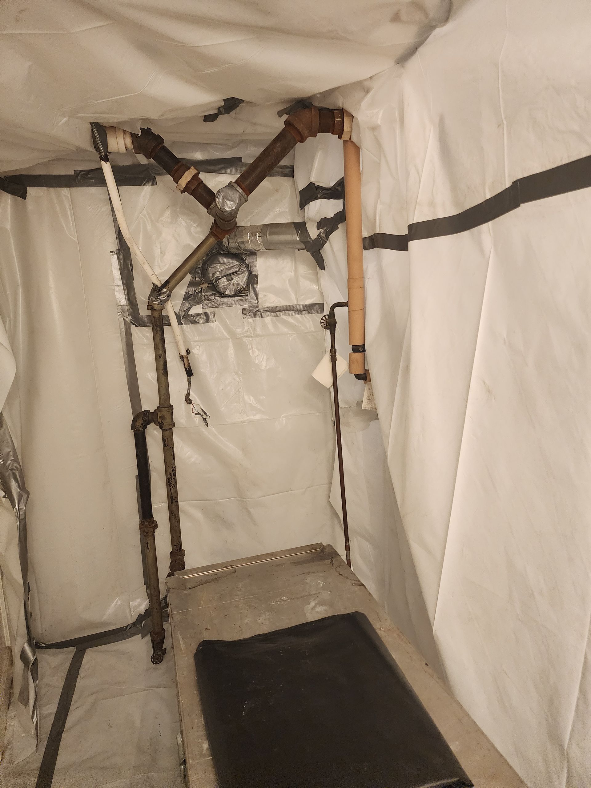 A medical examination room with a stainless steel examination table and overhead apparatus, covered in white plastic sheeting.