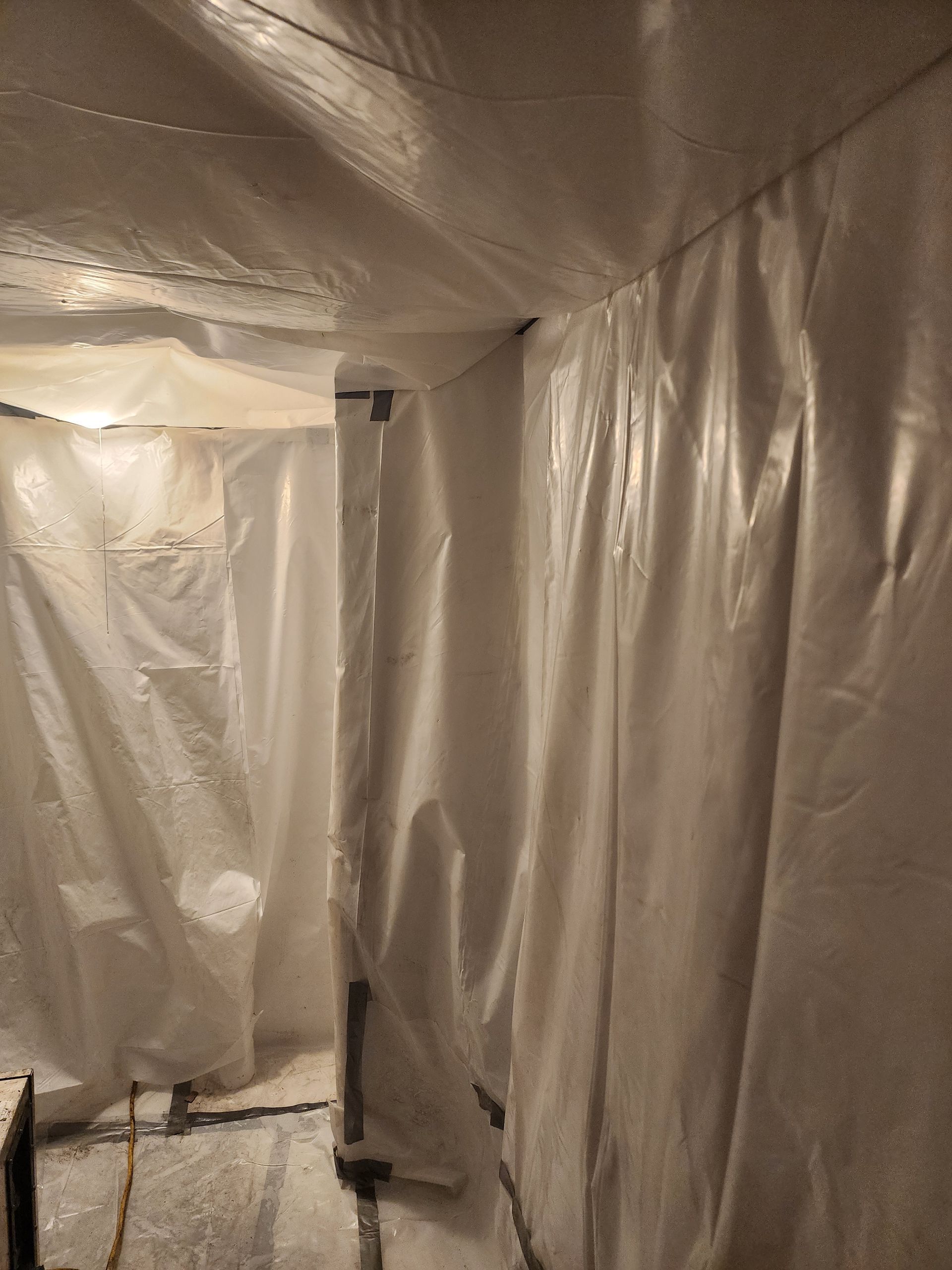 White plastic sheeting lines the walls and ceiling of a small, unfinished room.