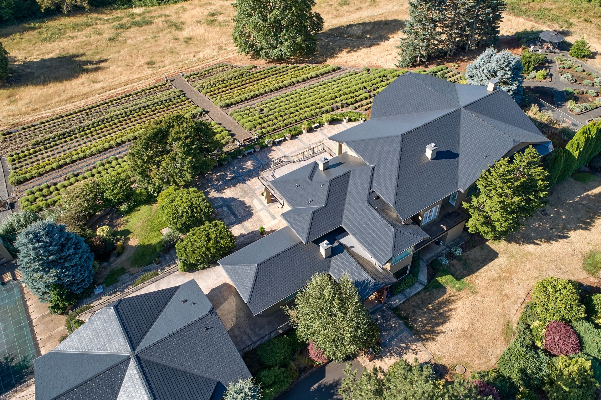 Overhead shot of a large residence with a newly installed black Interlock Slate aluminum roof in Mulino, OR 97042. The metal roofing system, installed by Interlock Metal Roofing, complements the surrounding farmland and lavender fields, and provides long-term protection from Oregon’s varied climate.