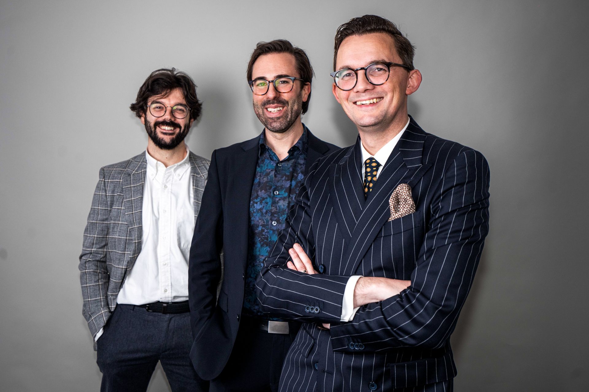 John Dobbin in blue suit writing at a table; smiling with glasses, orange pocket square.