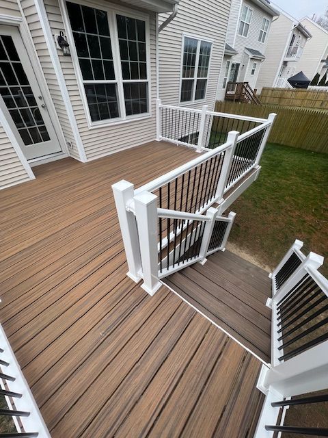 Backyard deck with white railing and stairs against a house with a brick chimney under a cloudy sky.