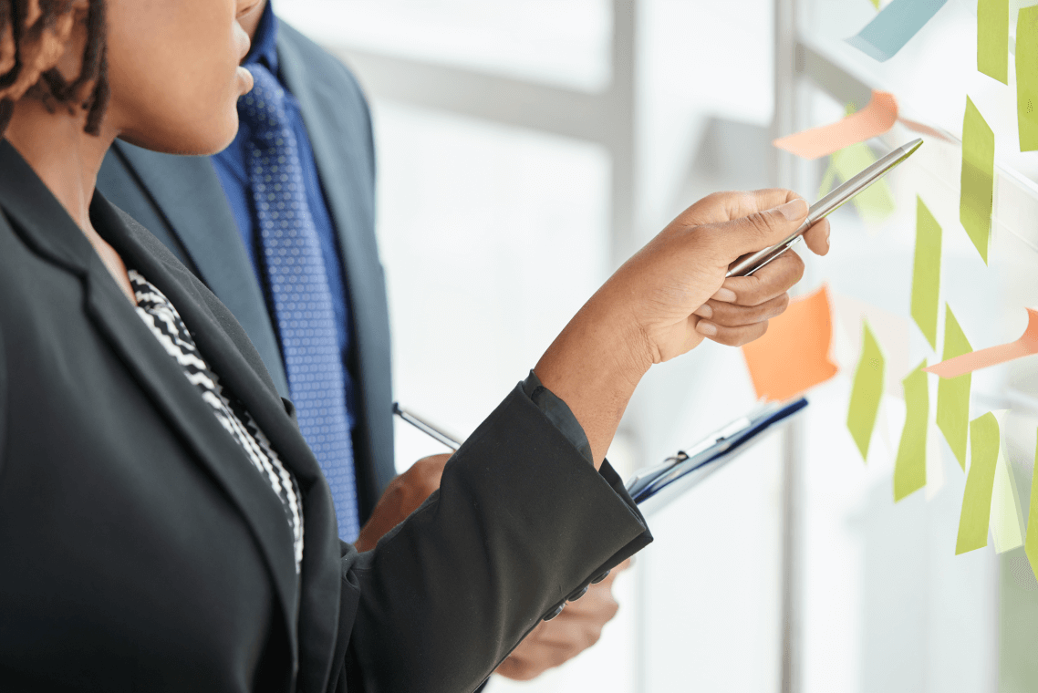 A man and a woman are looking at sticky notes on a wall.