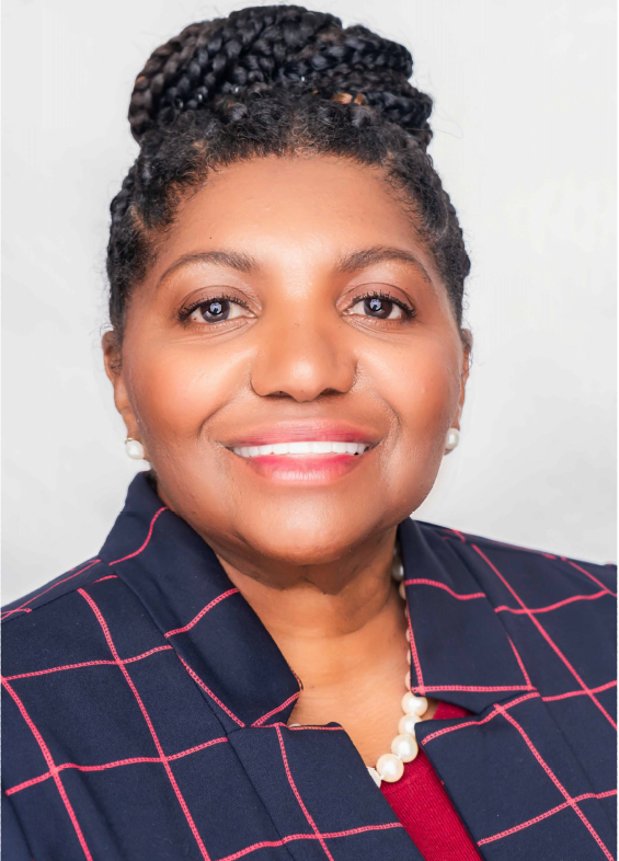 A woman wearing a plaid jacket and pearls smiles for the camera
