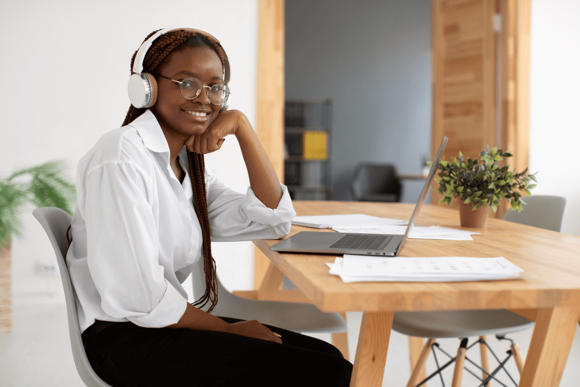 A woman wearing headphones is sitting at a table with a laptop.