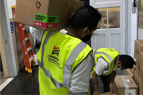 A man in a yellow vest is carrying a box on his shoulder.