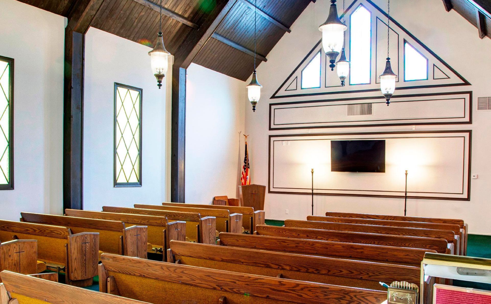 Interior of a chapel with wooden pews, white walls, and hanging lamps.