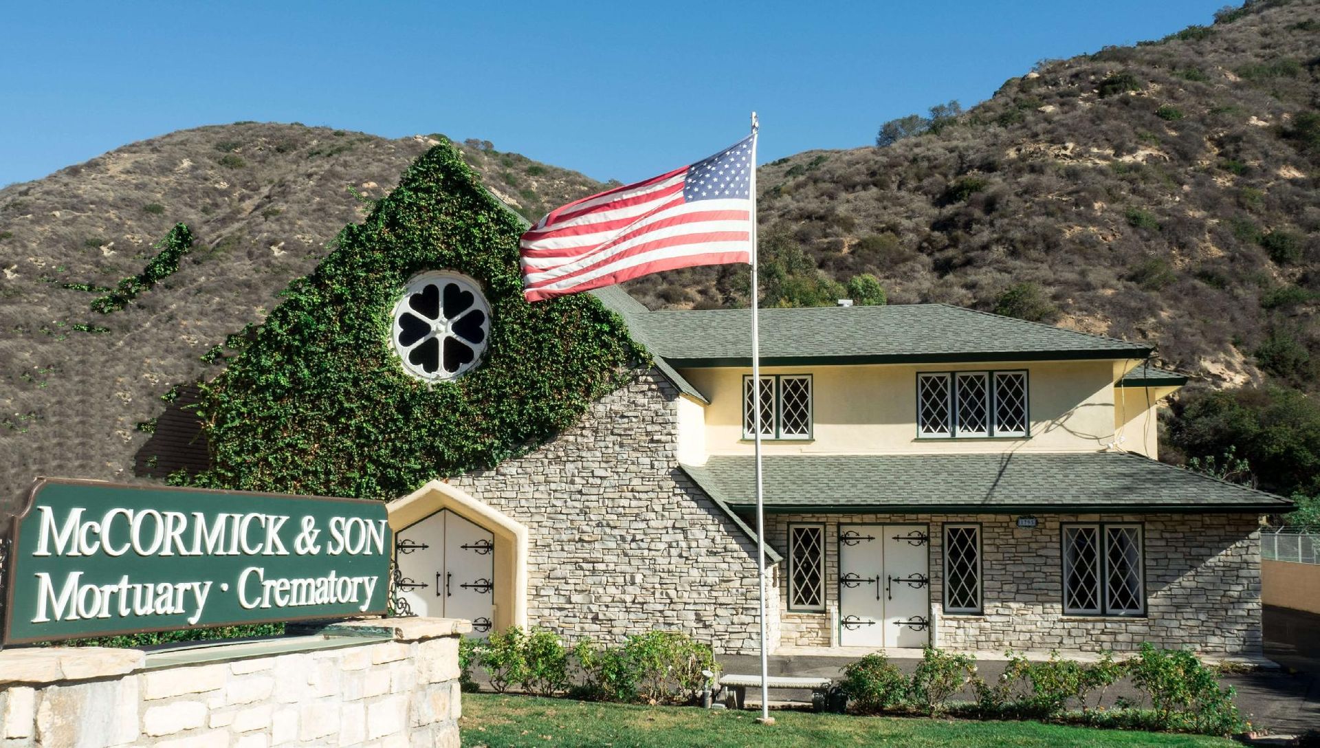 McCormick & Son Mortuary with American flag, ivy-covered wall, and mountain backdrop.