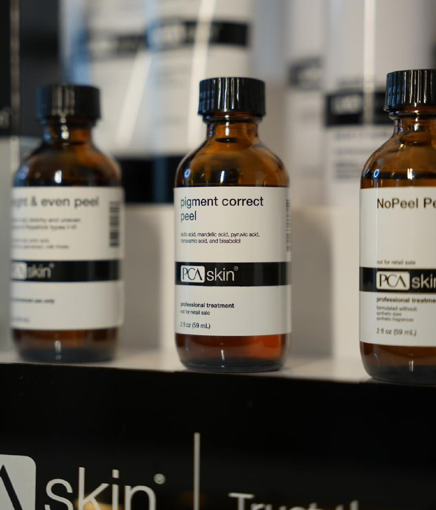 Three PCA skin product bottles on a shelf; amber glass, black caps, white labels.