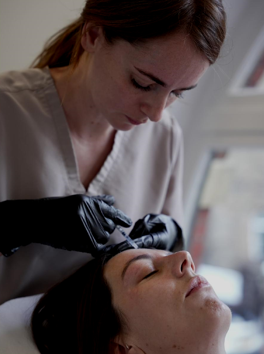 A woman receives a cosmetic injection on her forehead from a professional wearing gloves.
