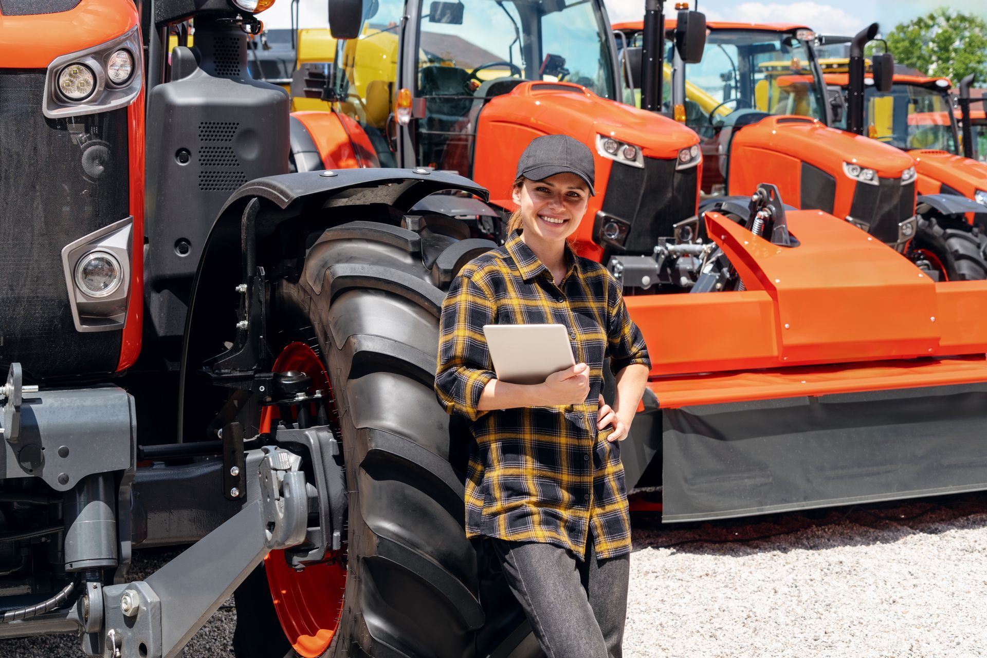 A representative at an agricultural machinery dealership stands next to a tractor & holds a tablet