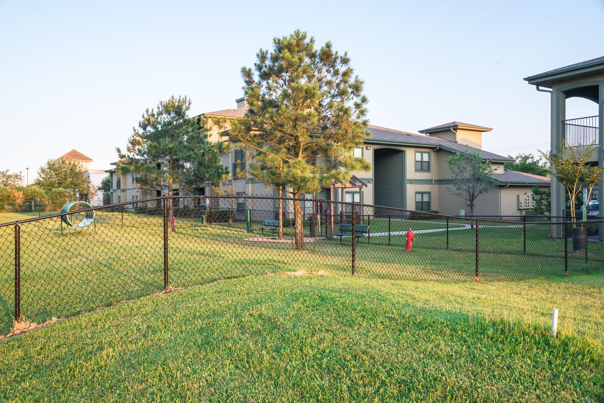 Chain-link fence enclosing a green lawn with pet play structures in a residential area.