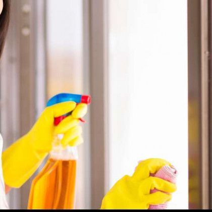 A woman wearing yellow gloves is cleaning a window with a spray bottle.