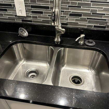 A stainless steel kitchen sink with a black counter top