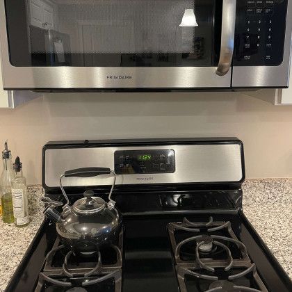 A stove with a tea kettle on it and a microwave above it.