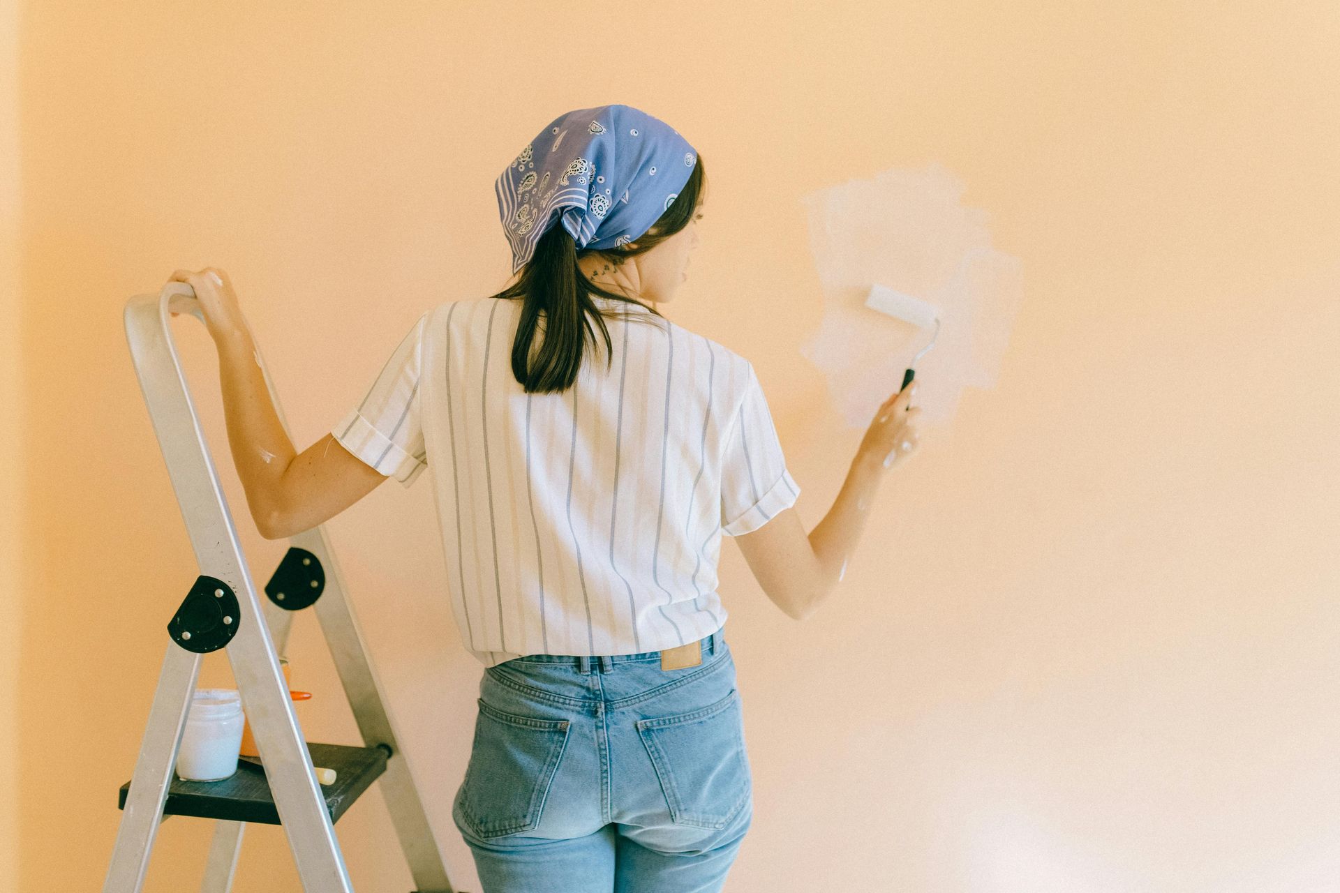 A woman is standing on a ladder painting a wall.