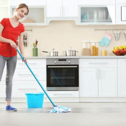 A woman is cleaning the floor in a kitchen with a mop and bucket.