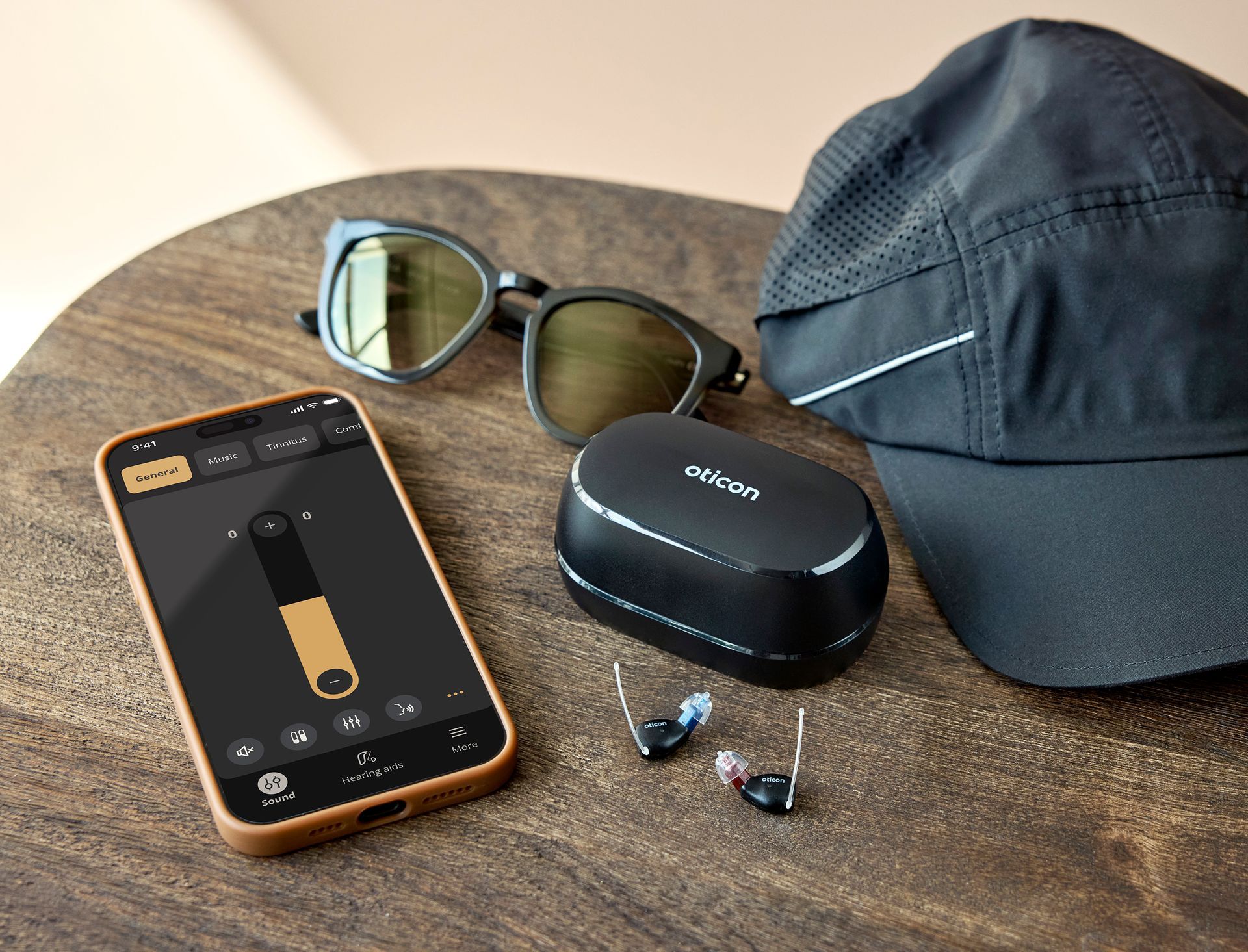 Sunglasses, earbuds, a black cap, and a phone on a round wooden table.