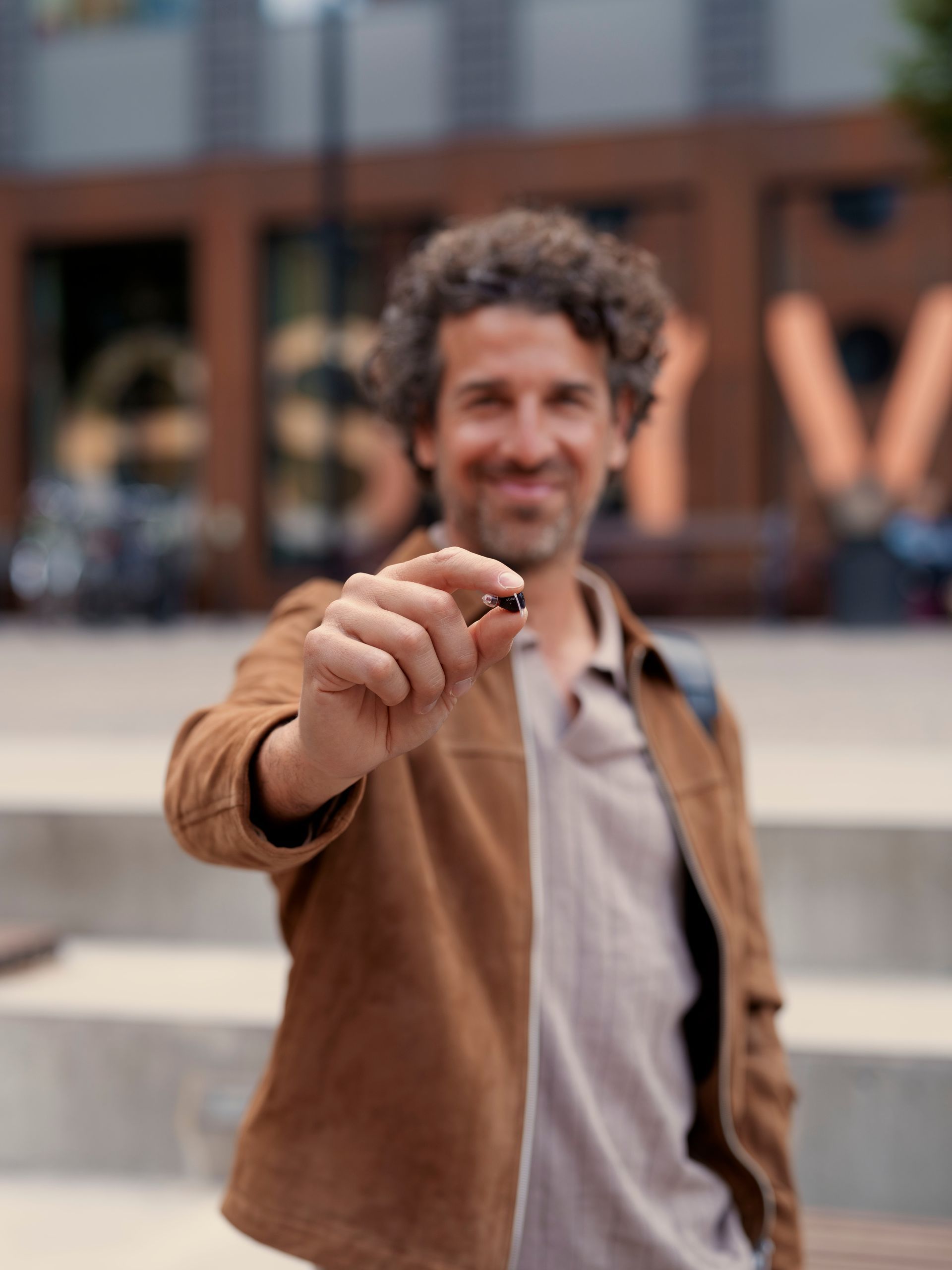 Man holding out a car key toward the camera outside a building