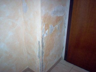 Un angolo di un muro con la vernice scrostata accanto a una porta.