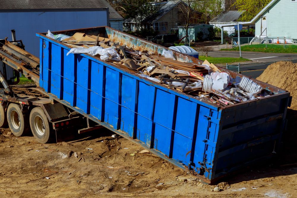 Blue Dumpster Filled With Debris Being Lifted by a Truck on a Construction Site — Mount Isa Skips In Camooweal, QLD