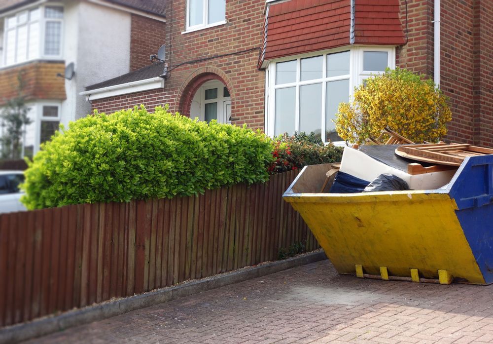 A Skip Filled With Debris Sits on a Driveway in Front of a Brick House — Mount Isa Skips In Camooweal, QLD