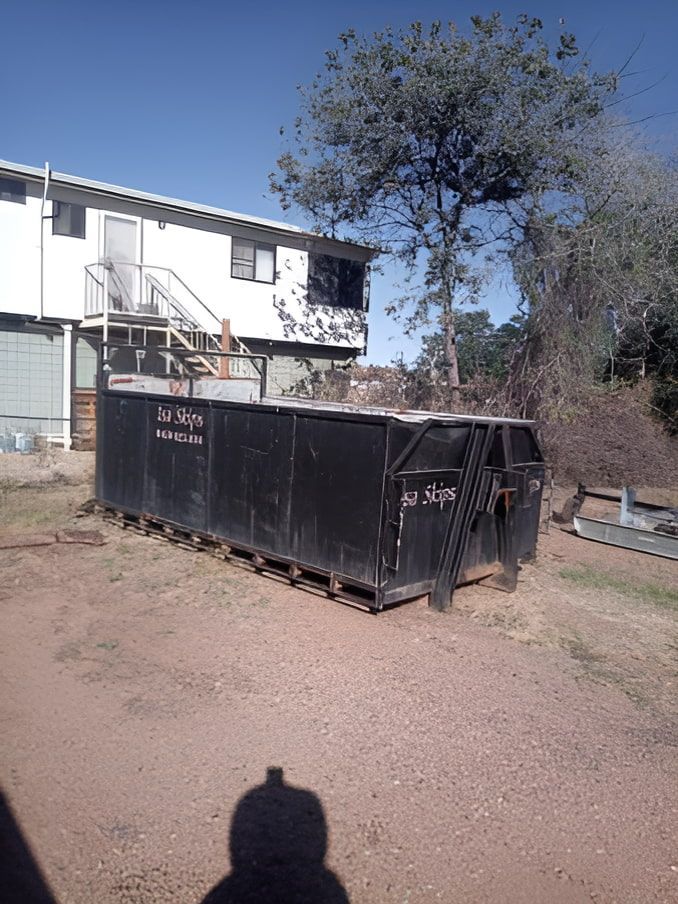 A Large Black Dumpster Is Sitting In Front Of A House — Mount Isa Skips In Mount Isa, QLD