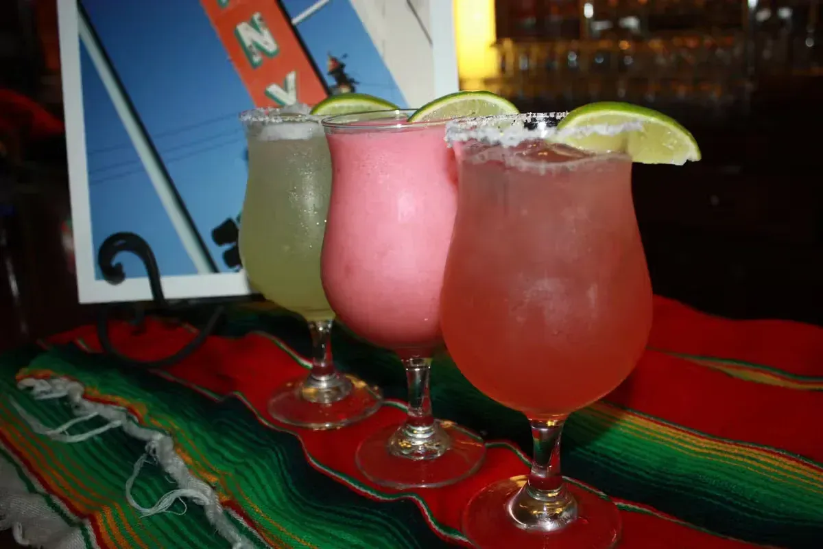 Three colorful cocktails with lime garnish on a Mexican blanket.