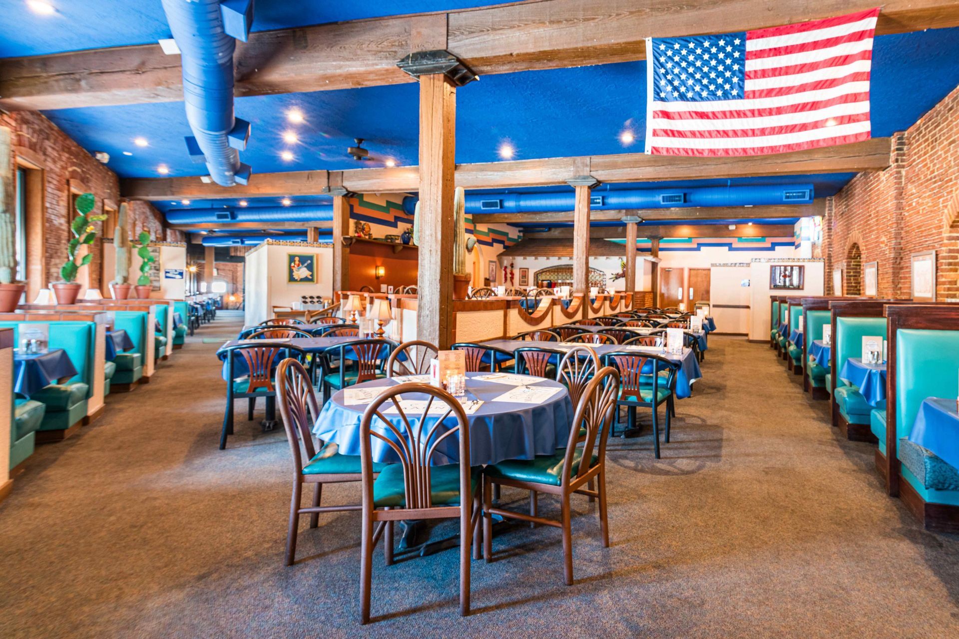 Restaurant interior with blue ceiling, booths, tables, American flag.