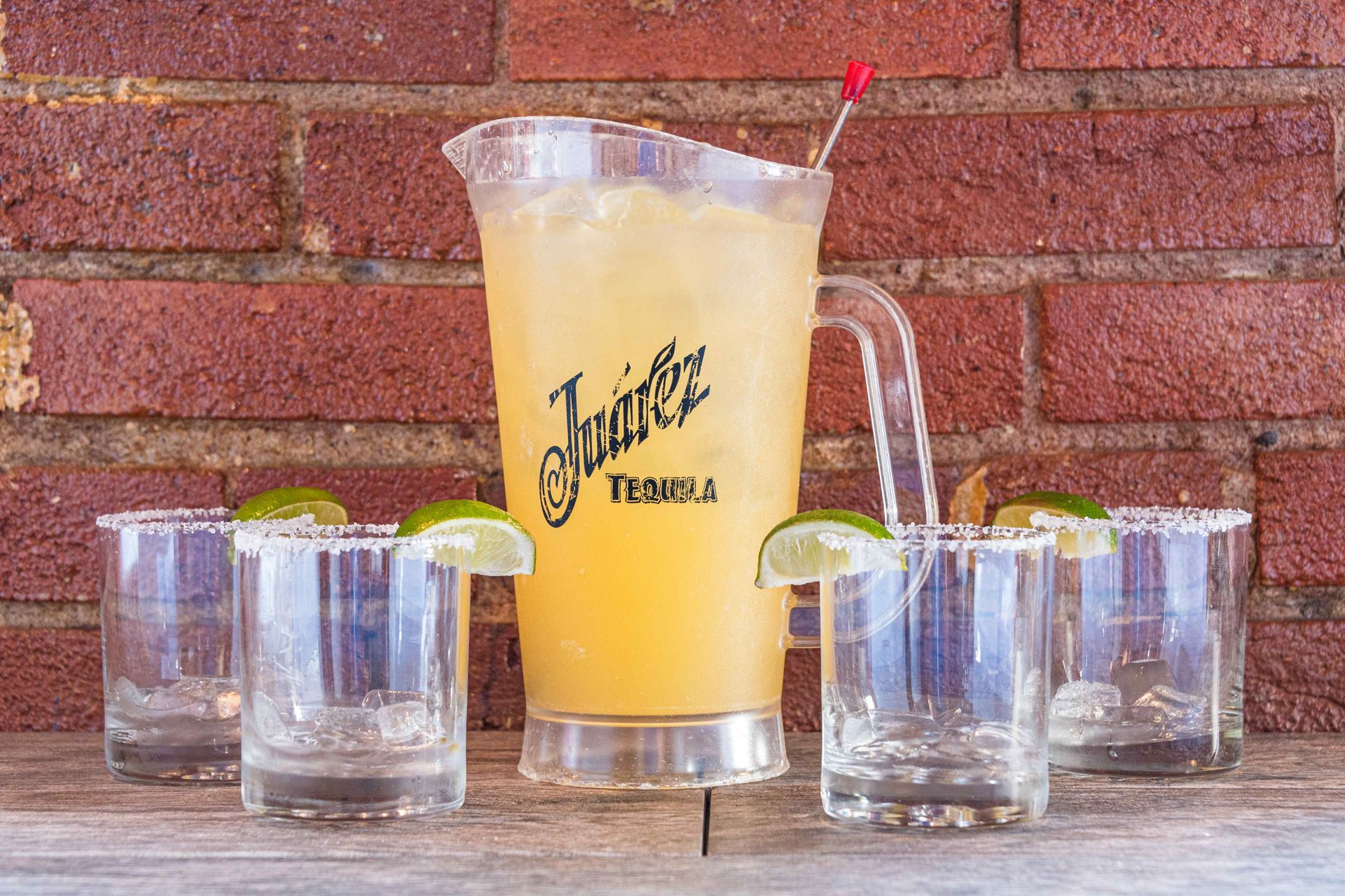 Pitcher and glasses of margarita on wooden table with brick wall background.