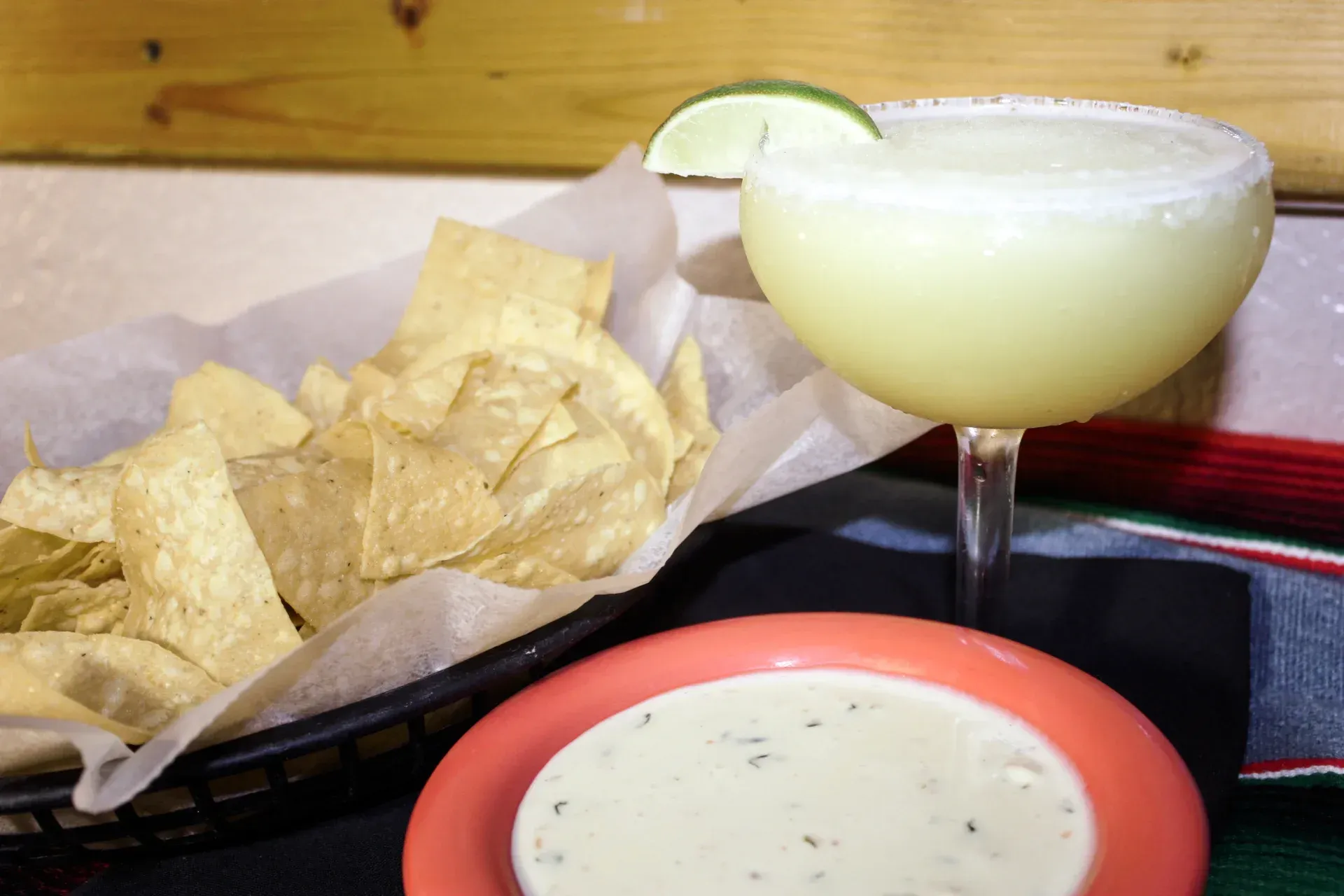 Margarita with lime garnish, chips, and white dip at a table in a restaurant.