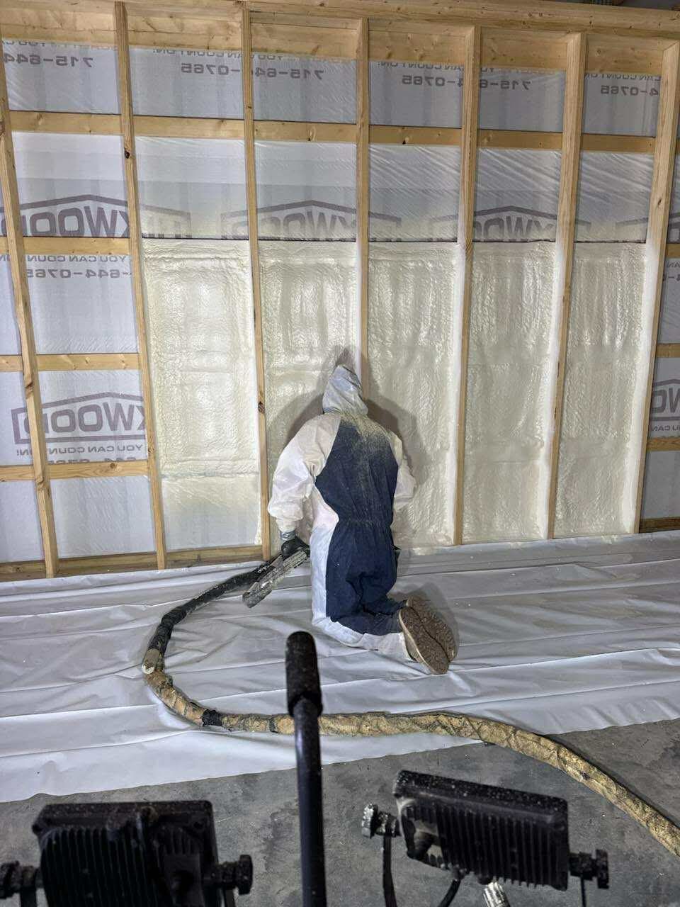 A person in a protective suit applies spray foam insulation