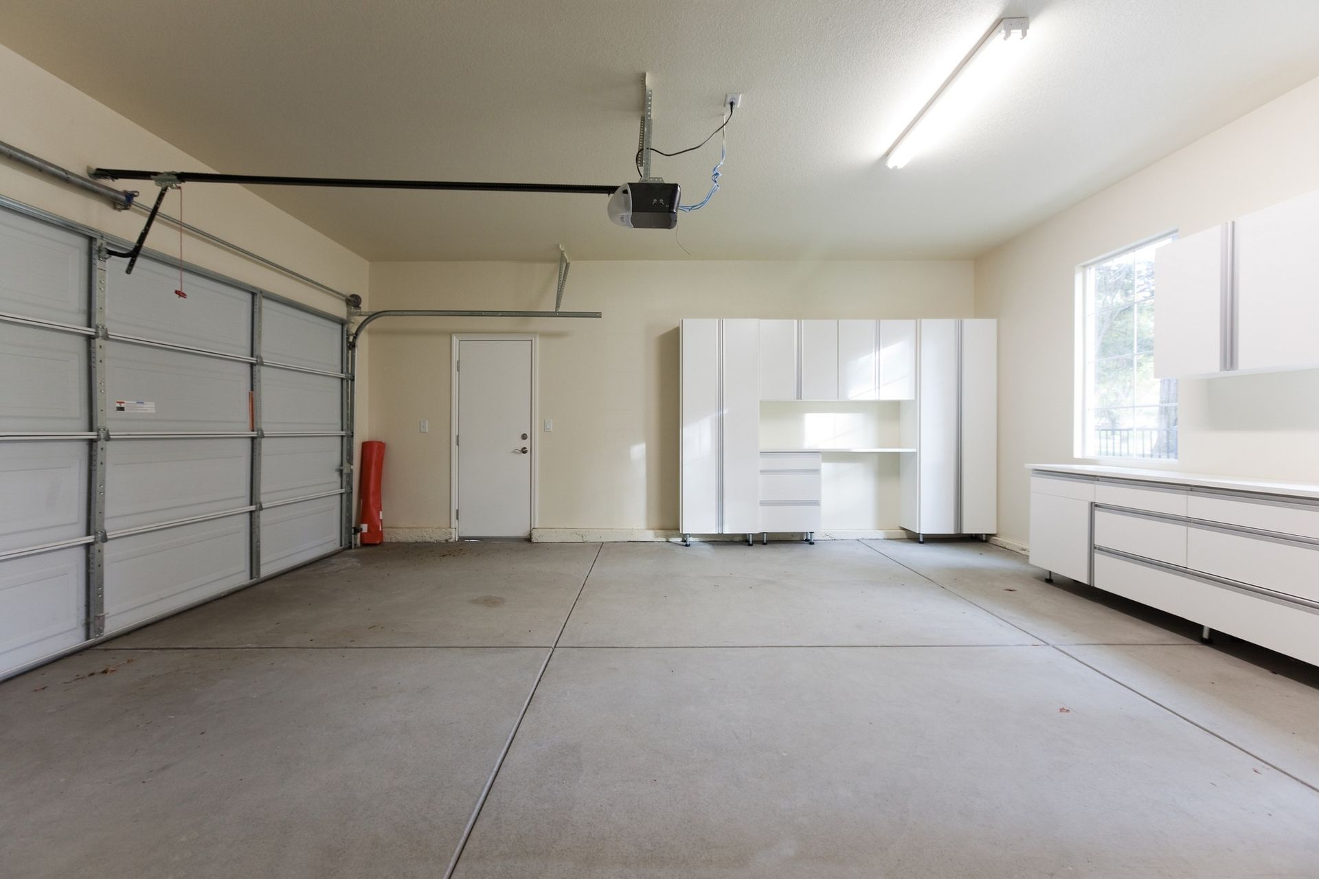 An empty garage with a garage door open and white cabinets.