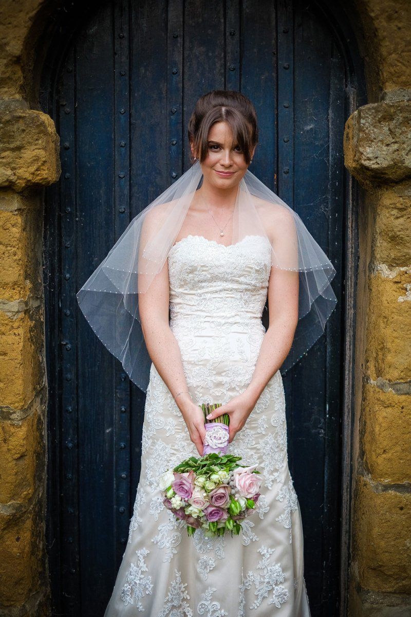 Bride in white strapless dress holding a bouquet, standing in front of a blue arched door.