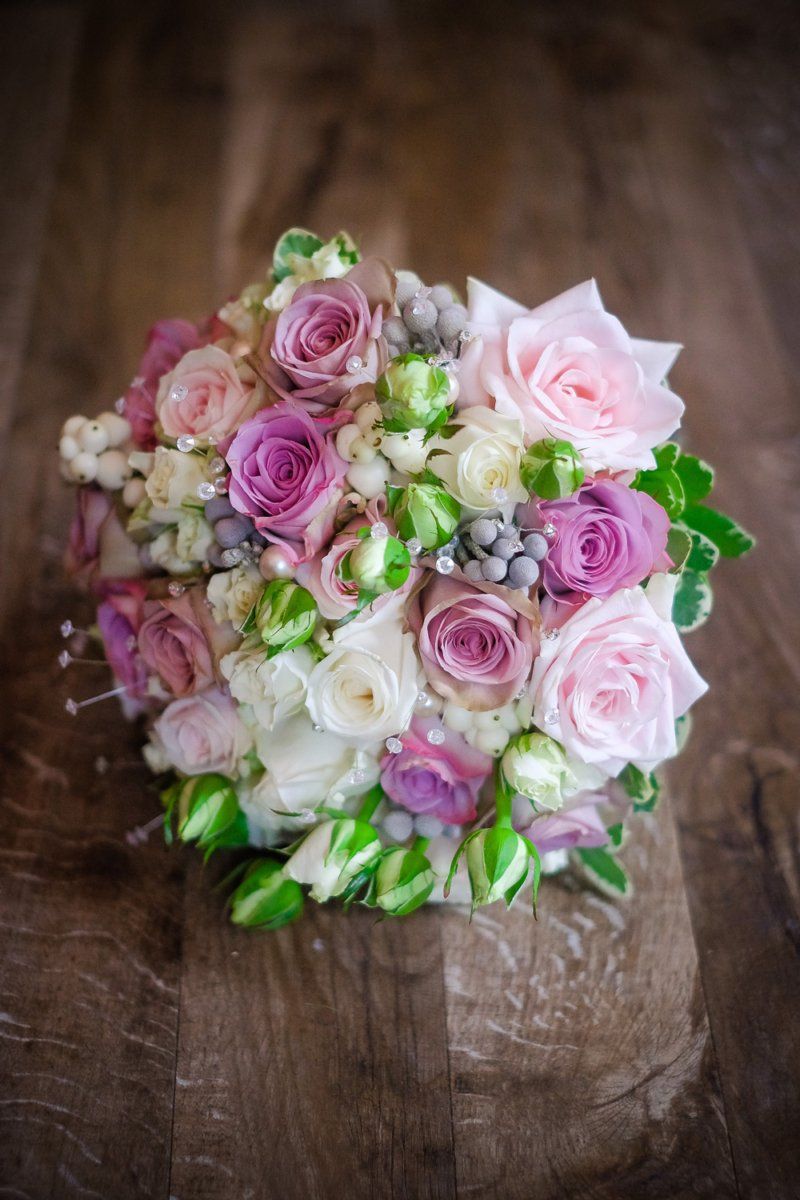 Bouquet of pink and purple roses and white flowers, with green accents, on a wooden surface.