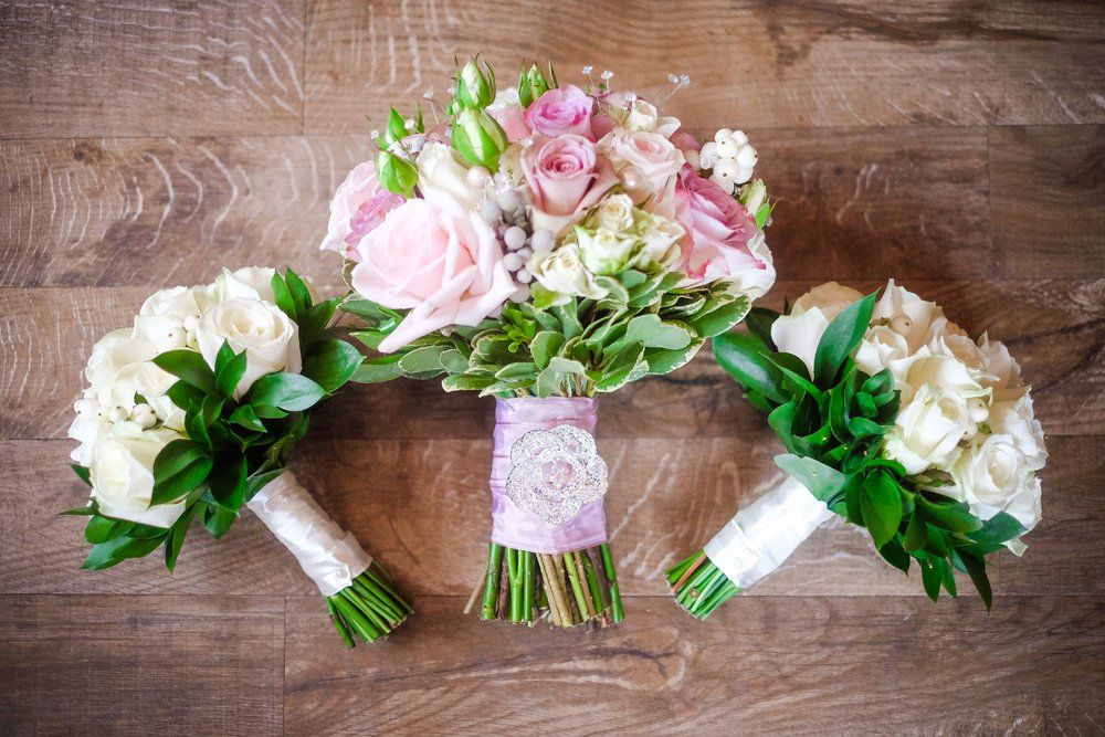 Three bridal bouquets with white and pink roses on a wood surface.