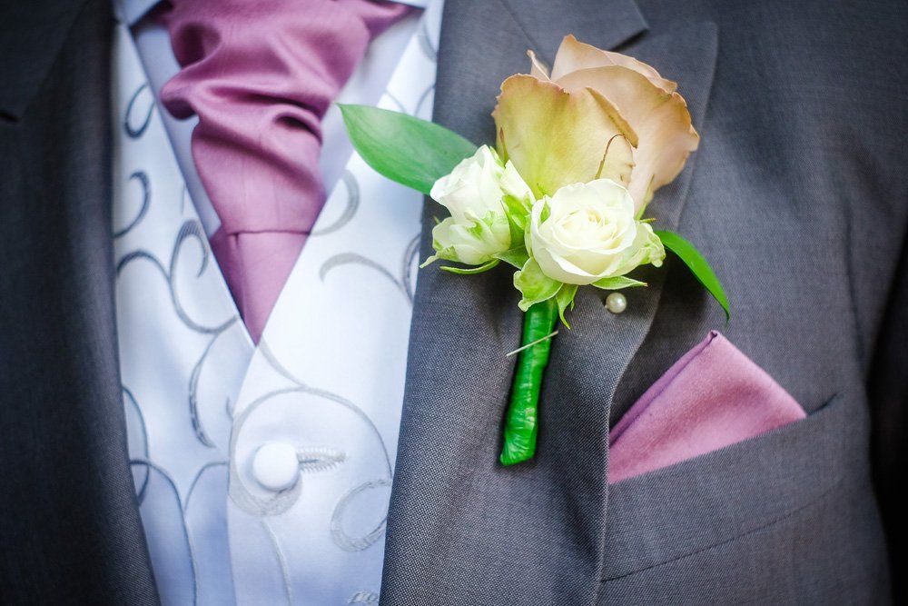 Groom's boutonniere of white and peach flowers, with matching pocket square, on a gray suit.