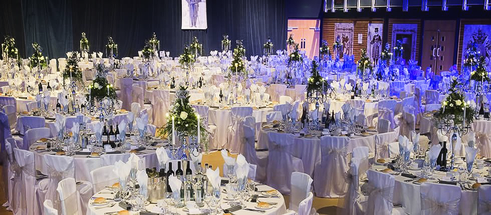 Formal dining tables set up in a large hall, decorated with flowers and centerpieces.