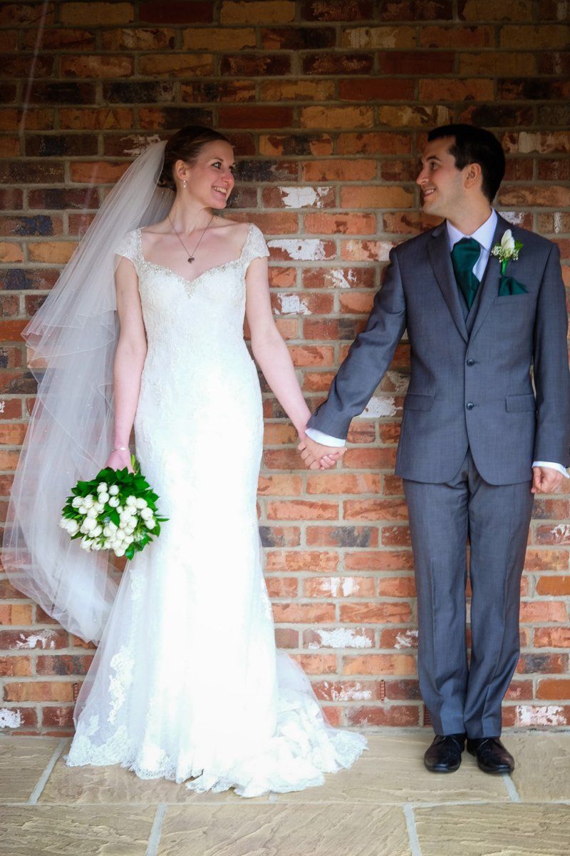 Bride and groom holding hands, smiling, in front of a brick wall.