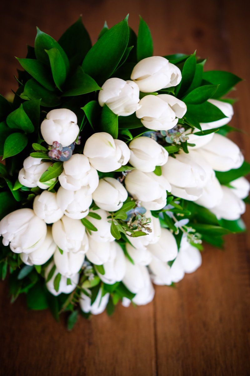 White tulip bouquet with lush green foliage on wooden surface.