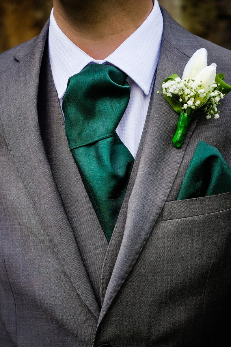 Man in gray suit with a green necktie, pocket square, and boutonniere.