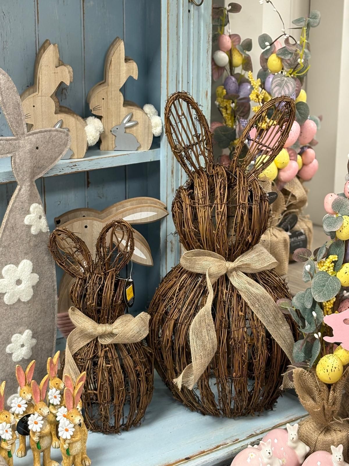 Easter bunny decorations, woven brown, with burlap bows, on a shelf with other holiday decor.