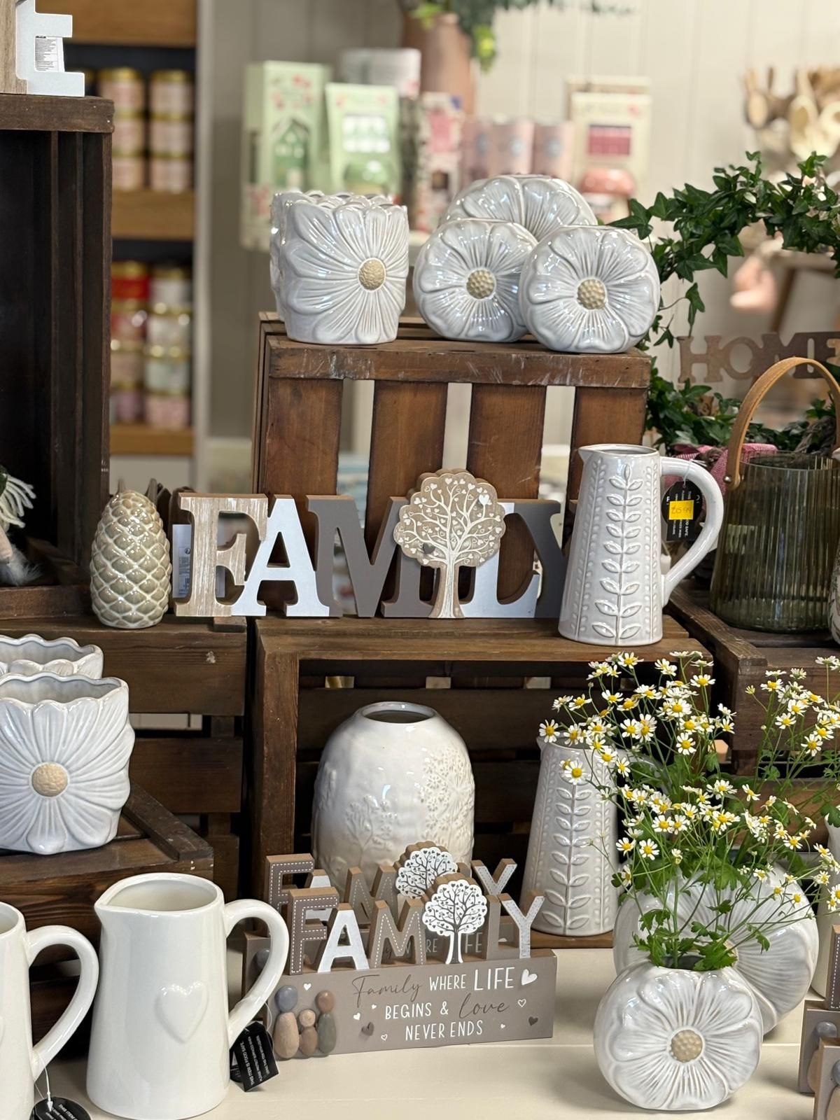 Display of white ceramic vases, pots, and a Family sign, set on wooden crates in a store.