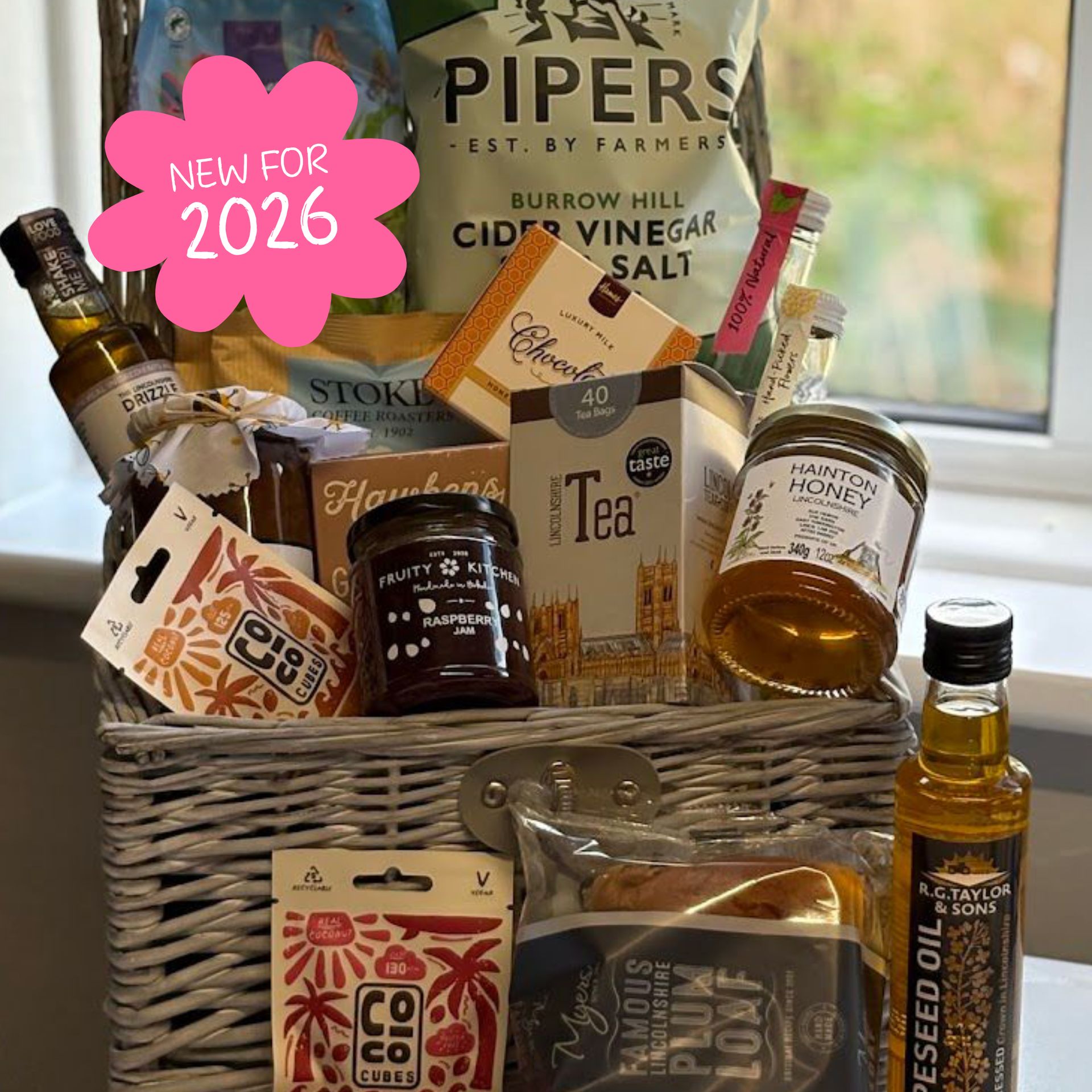 Wicker gift basket filled with food items including snacks, tea, honey, and oil. 