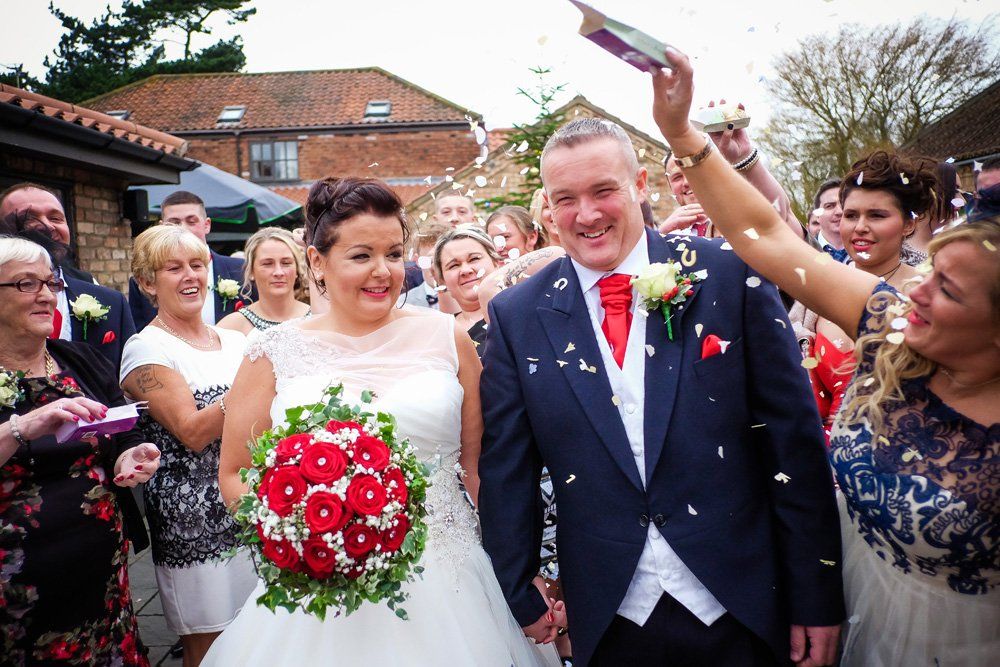 Newlyweds smiling, showered with confetti after their wedding ceremony.